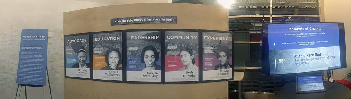 Panorama of museum exhibit's introductory board on poster stand, 5 civil rights leaders posters hung on a large board, and a screen displaying a timeline.